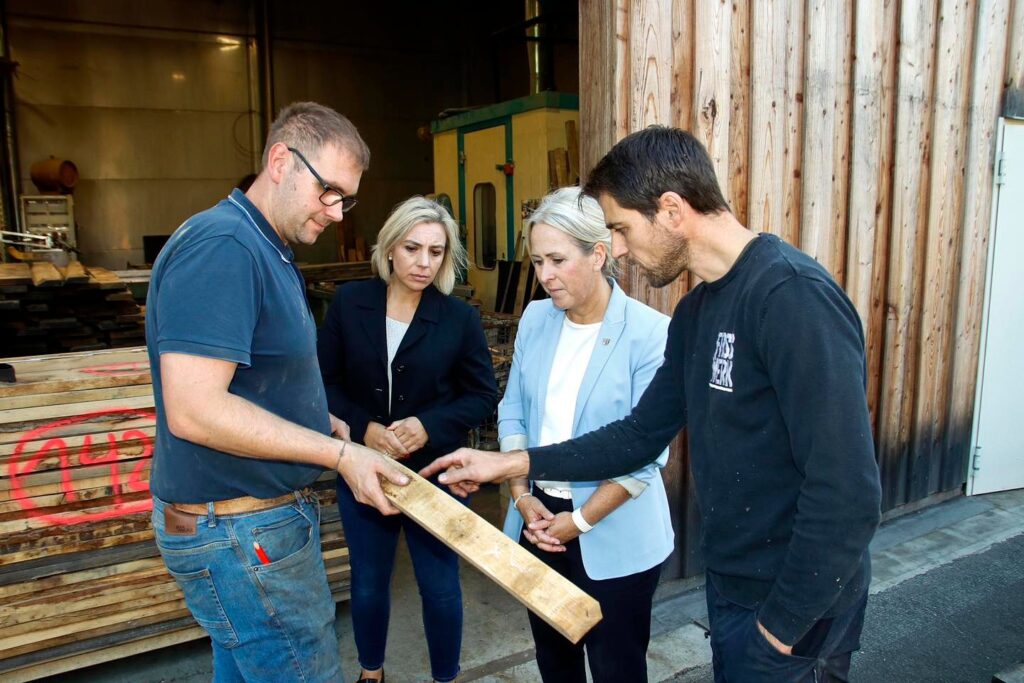 Zwei Frauen und zwei Männer begutachten ein Stück Holz für die Verarbeitung zu einem Fass. Sie stehen vor einem Holzlager.