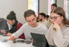 Zwei Schüler sitzen mit einem Tablet und arbeiten konzentriert, während andere im Hintergrund zu sehen sind.