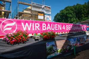 Banner Wir bauen vier Bergvillen ist vor dem Rohbau zu sehen